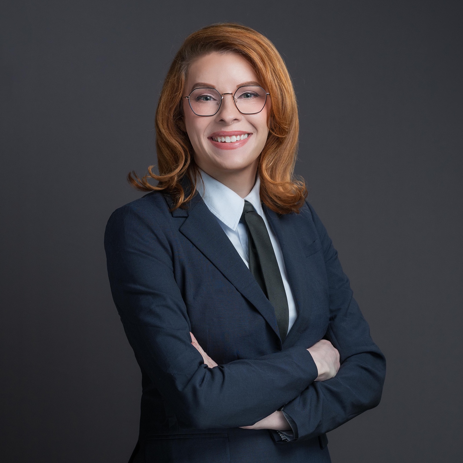 Danni Askini in navy suit with green tie, arms crossed